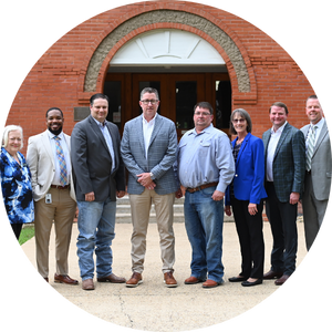 8 adults in front of entrance to brick building